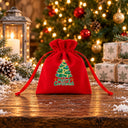 Sacchettino regalo in velluto rosso con motivo Buon Natale, su un tavolo rustico innevato davanti all’albero illuminato