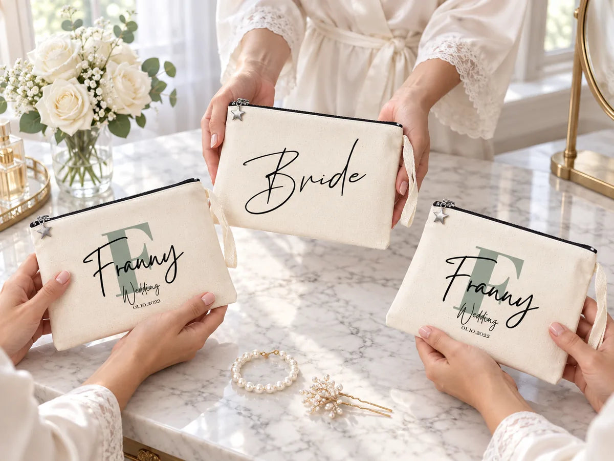 Mani di damigelle in vestaglie di seta su una toeletta di marmo con la pochette «Bride» e due pochette «Franny Wedding» in cotone naturale, rose bianche e un bracciale di perle