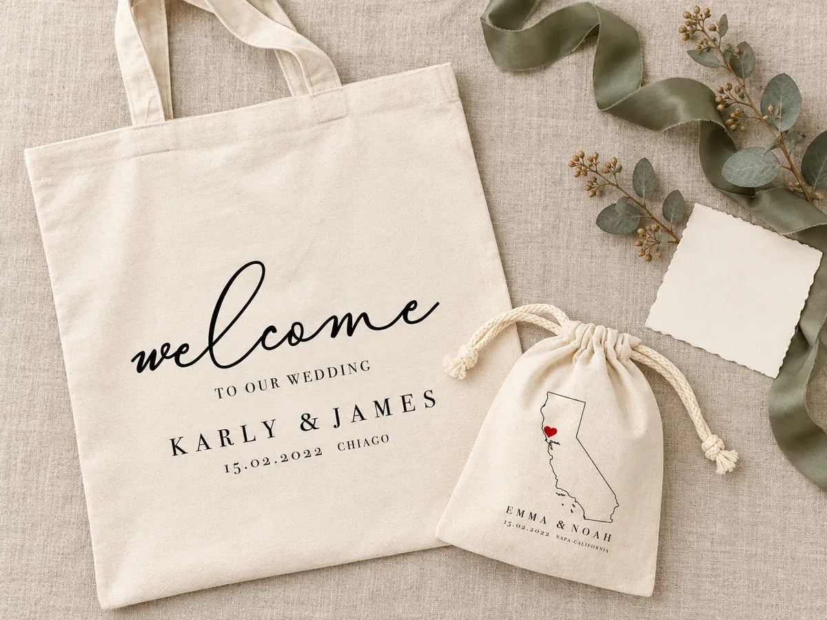 Flat-lay dall'alto su lino: la tote bag «Karly & James» e il sacchetto con la mappa della California, un nastro di seta verde salvia, eucalipto essiccato e un cartoncino avorio